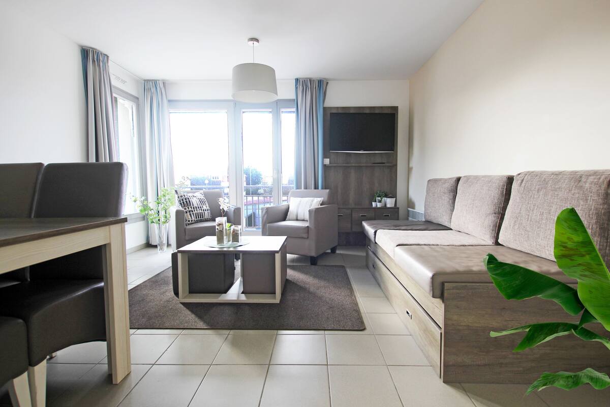 Una sala de estar moderna con un sofá, una mesa de comedor y un televisor montado en la pared.