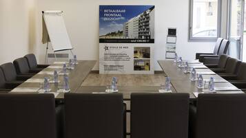 A conference room with a long table, chairs, water bottles, and a poster advertising a hotel.