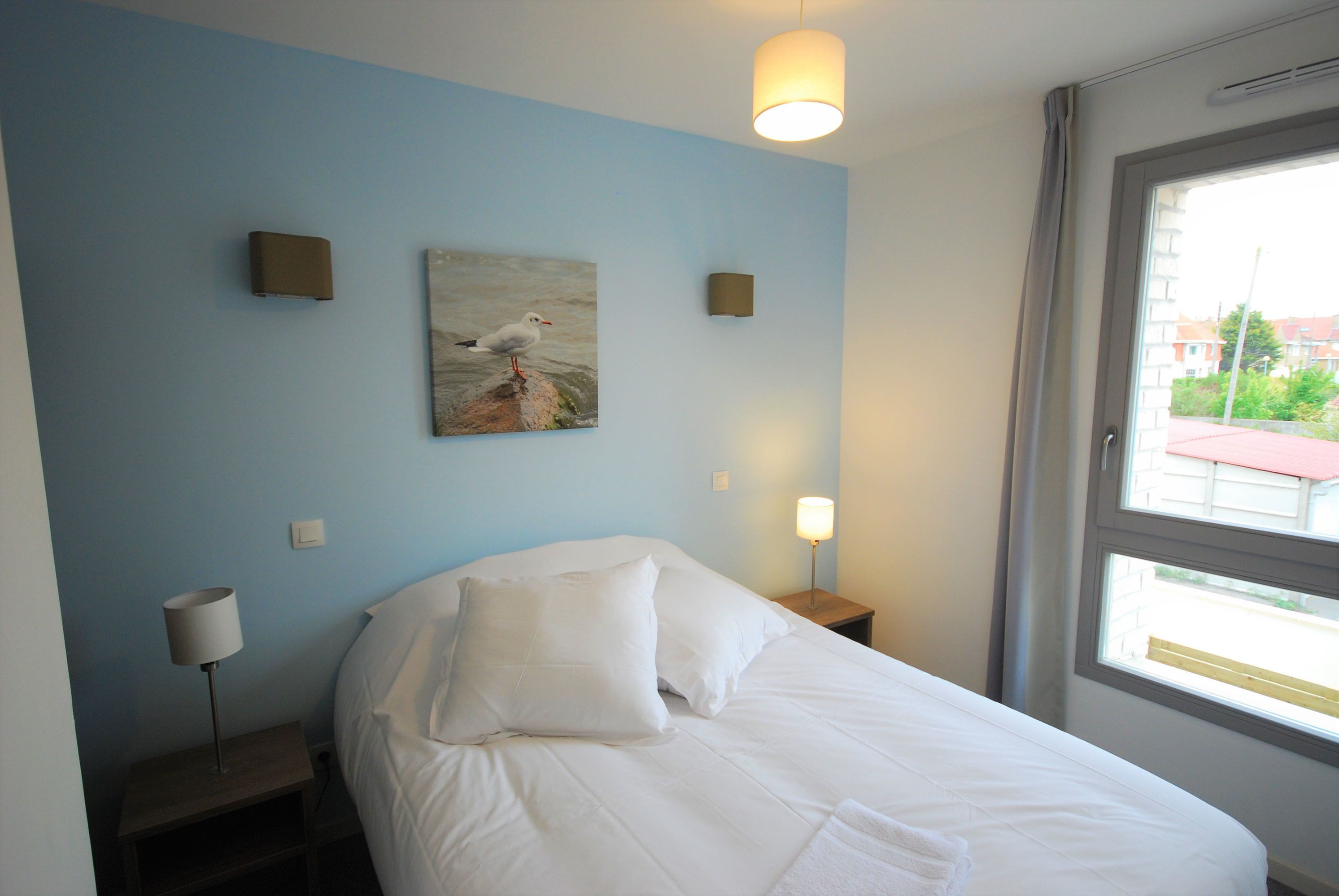 Une chambre à coucher avec un lit, un tableau, une table de chevet, une lampe et une fenêtre.