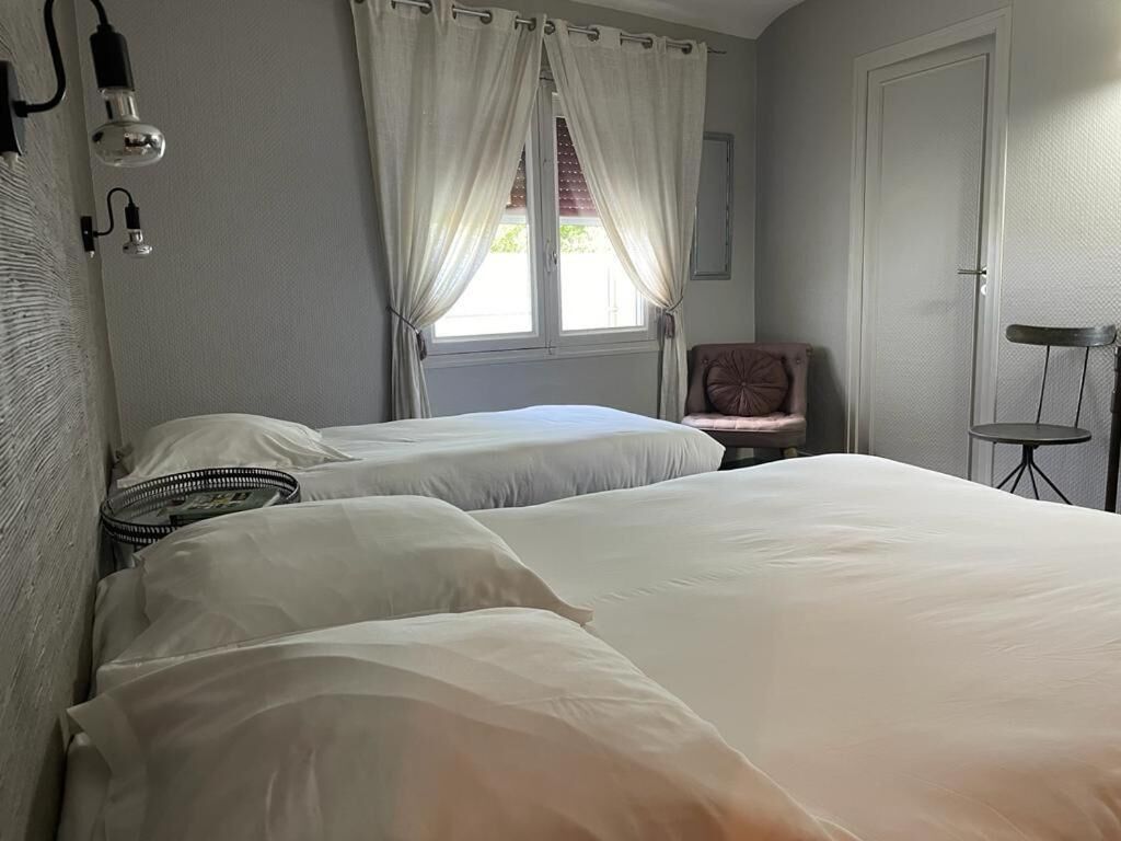 A bedroom with two beds, a chair, a small table, and a window with curtains.