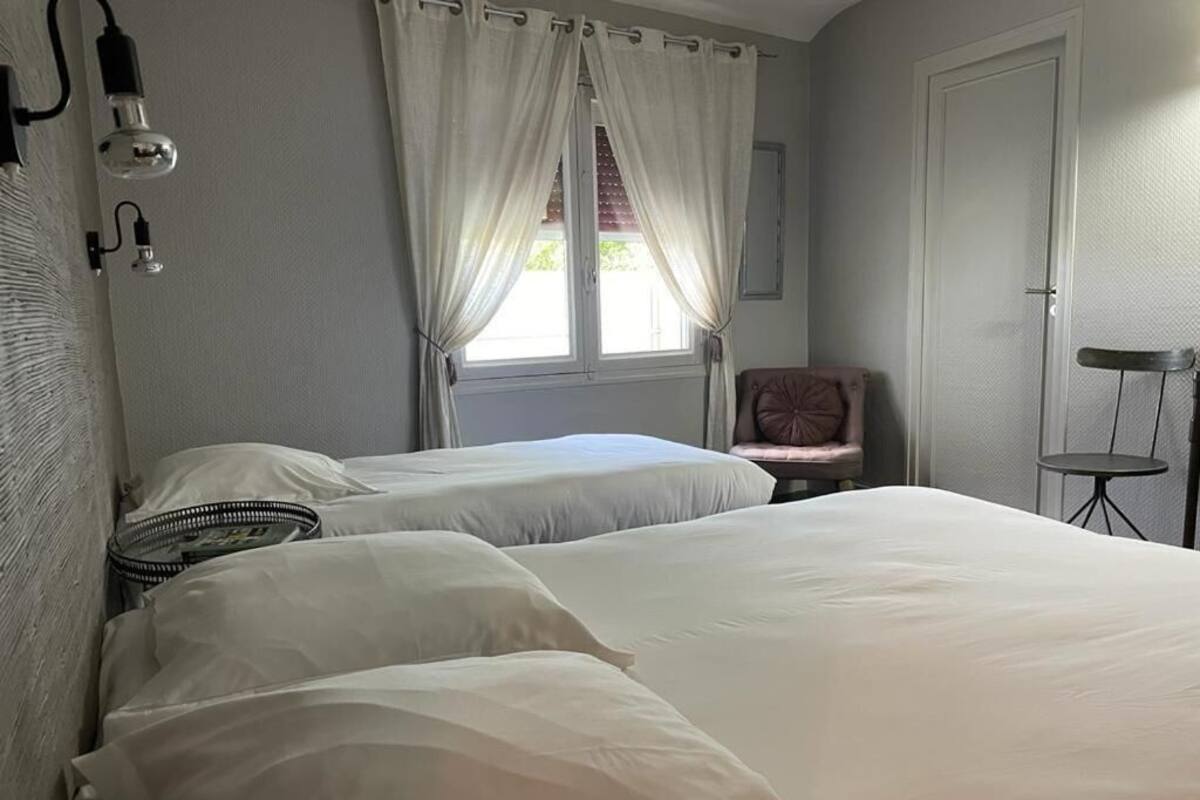 A bedroom with two beds, a chair, a small table, and a window with curtains.