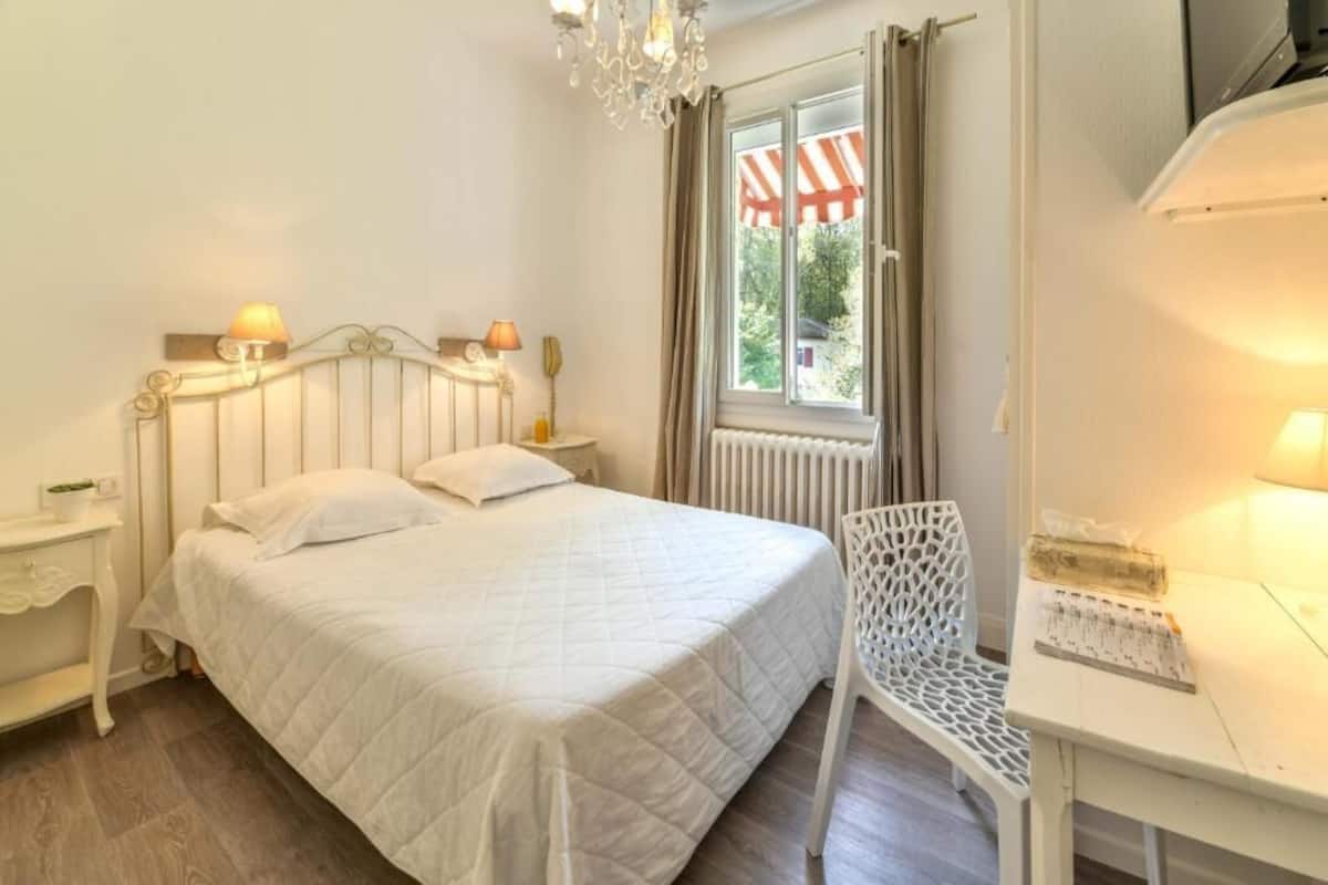 A bedroom with a bed, bedside tables, a chair, a window with curtains, and a radiator.