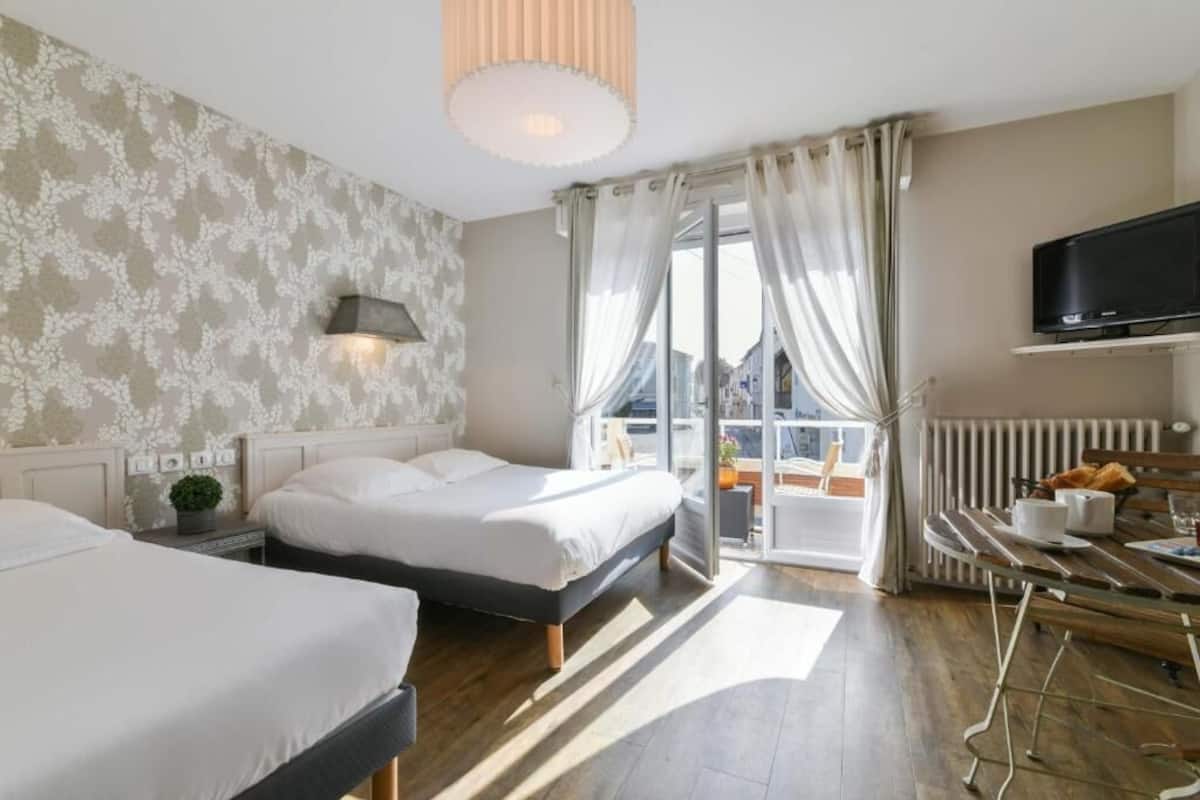 A hotel room with two beds, a TV, a dining table, and a view of the city.