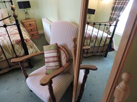 A bedroom with a wooden rocking chair, a bed with floral bedding, a nightstand, and a lamp.