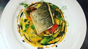 A white plate with a fish, vegetables, and sauce. - The Angel B&B (Aylesbury)
