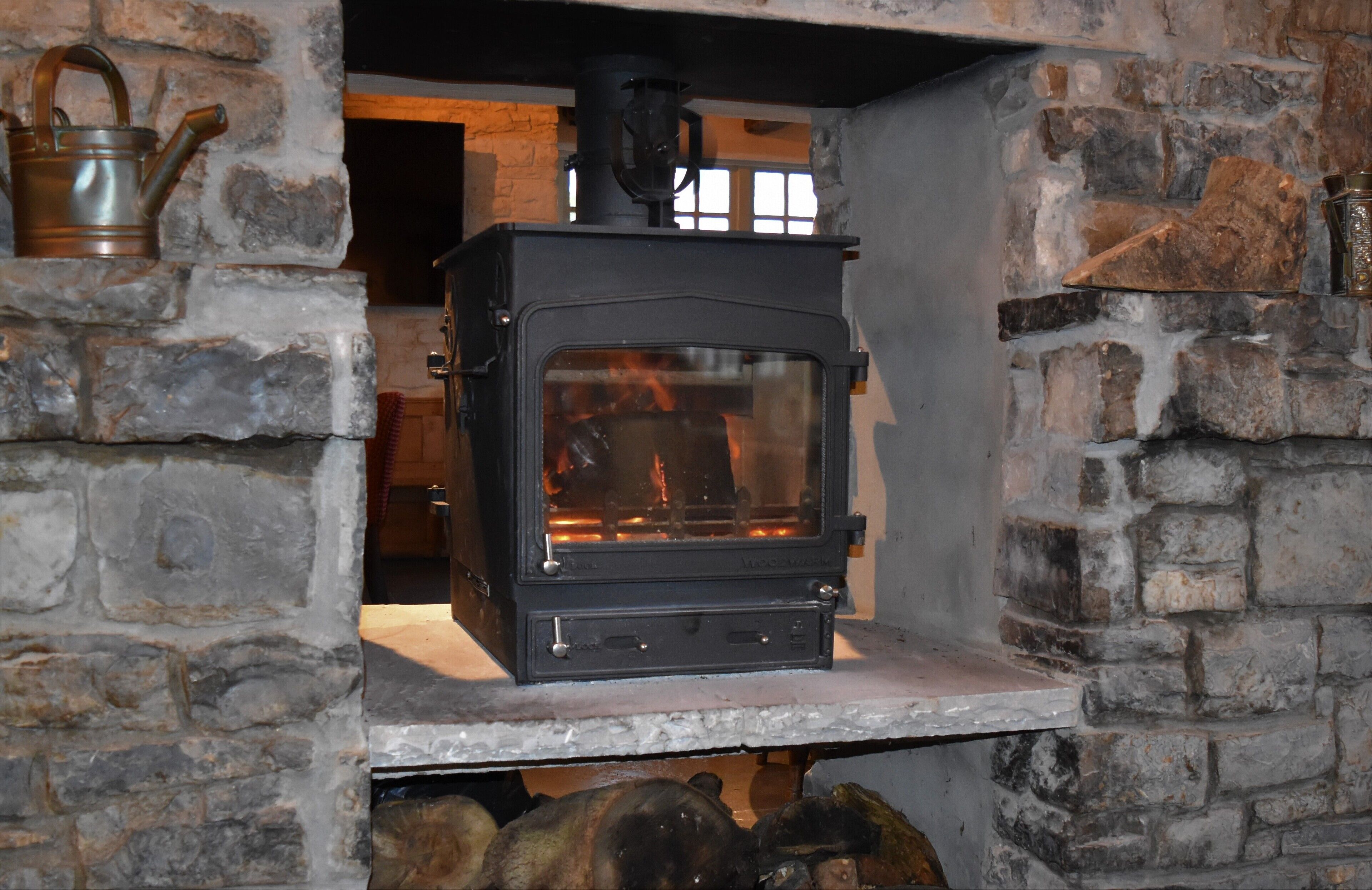 A wood-burning stove in a stone-walled room with a shelf below.