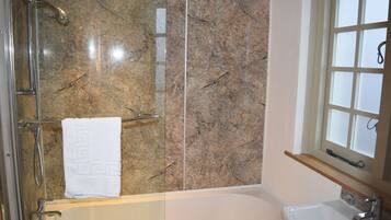 A bathroom with a marble wall, a bathtub, a sink, and a window with frosted glass.