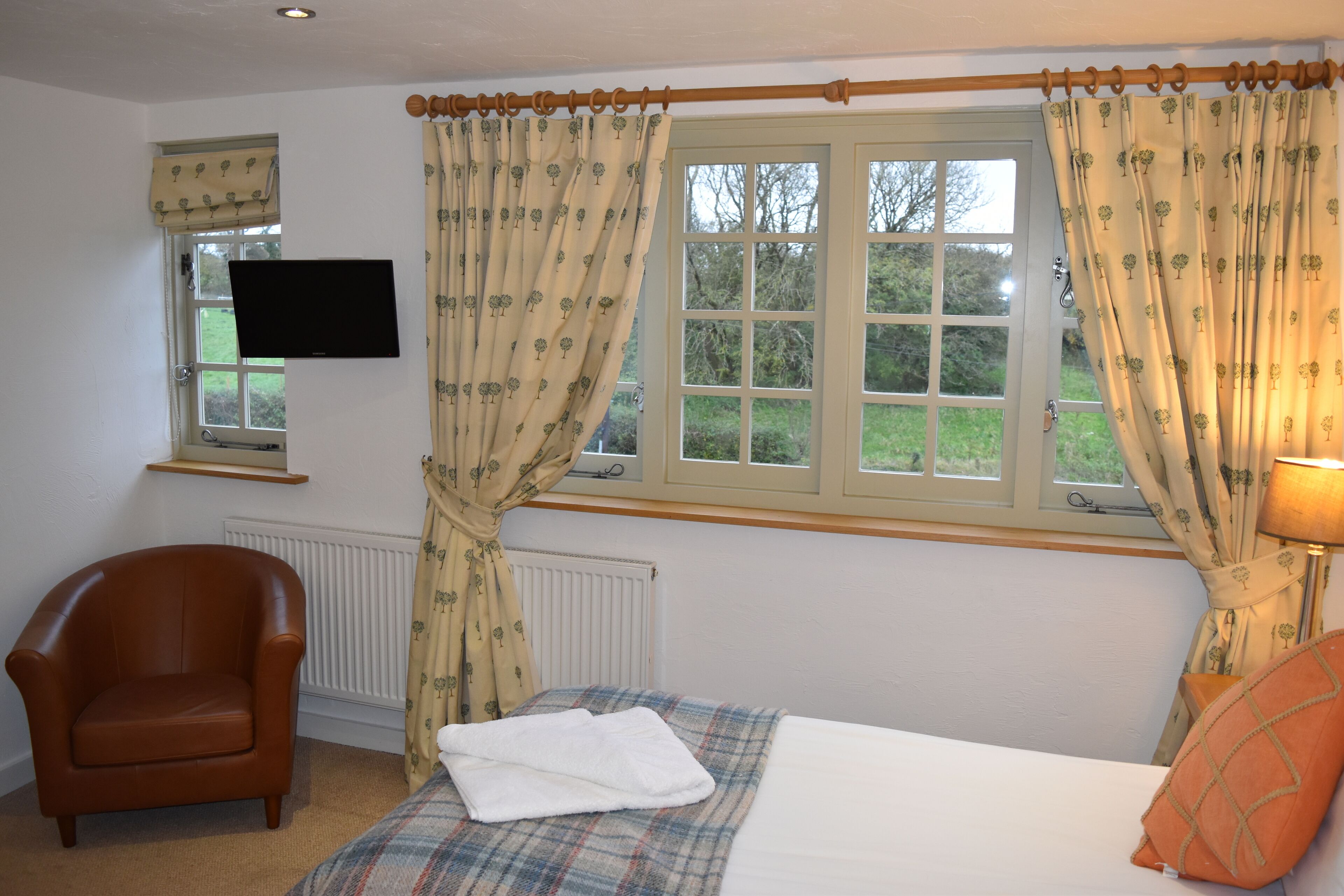 A bedroom with a bed, a chair, a TV, and a window with curtains.
