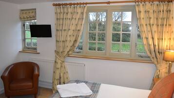 A bedroom with a bed, a chair, a TV, and a window with curtains.