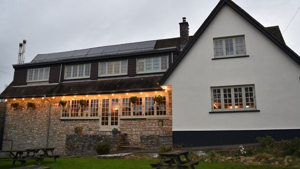A two-story building with a stone facade and a white upper section. There are multiple windows, some with shutters, and a small porch area with hanging flower baskets. - Three Horseshoes (Barry)