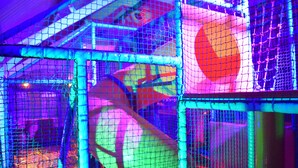 A brightly lit indoor play area with colorful structures and netted safety barriers. - Three Horseshoes (Barry)