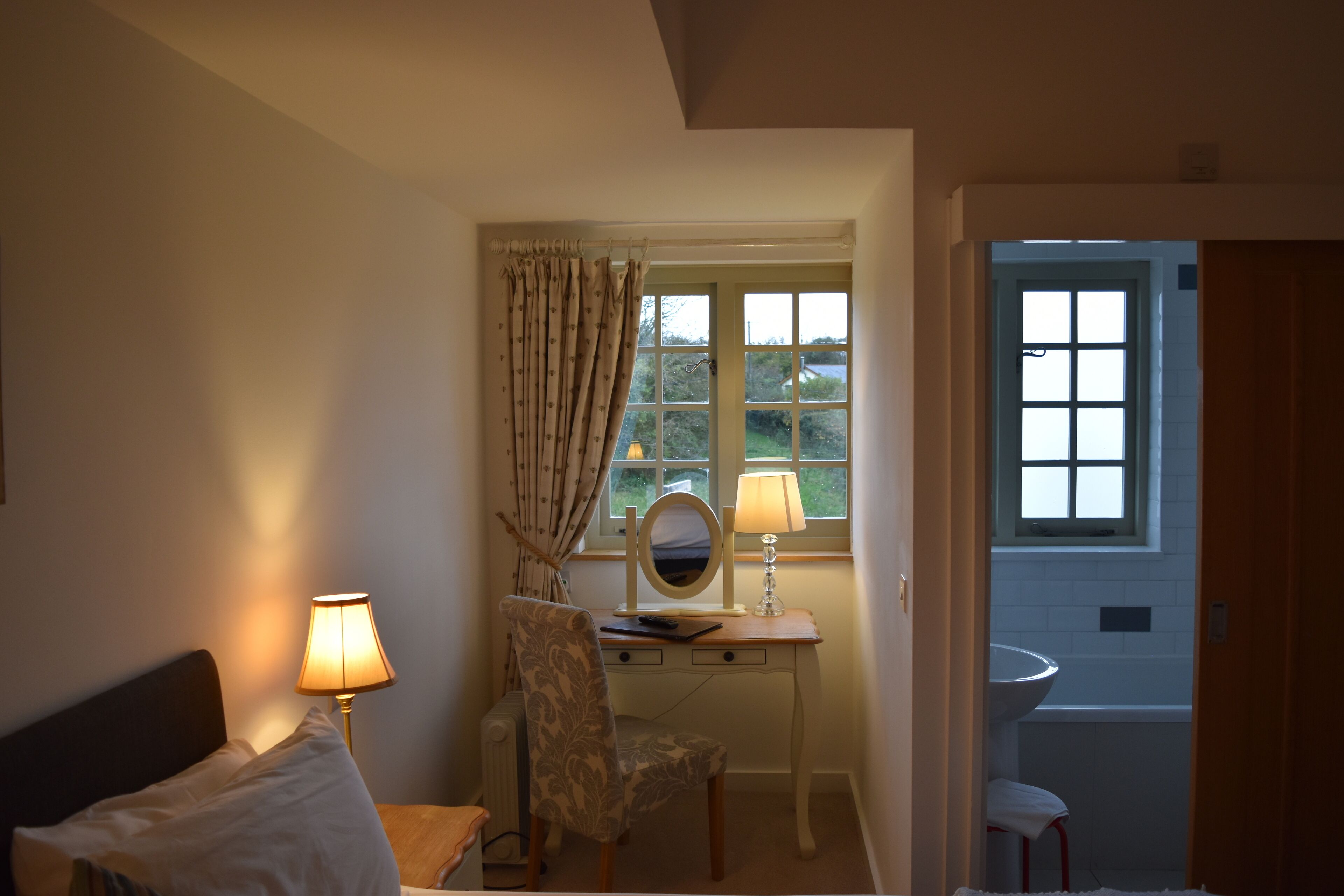 Un dormitorio con cama, un escritorio con espejo, una lámpara y vistas al baño.