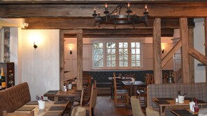 A rustic interior with wooden beams, a chandelier, and a view of the outdoors through large windows. - Three Horseshoes (Barry)