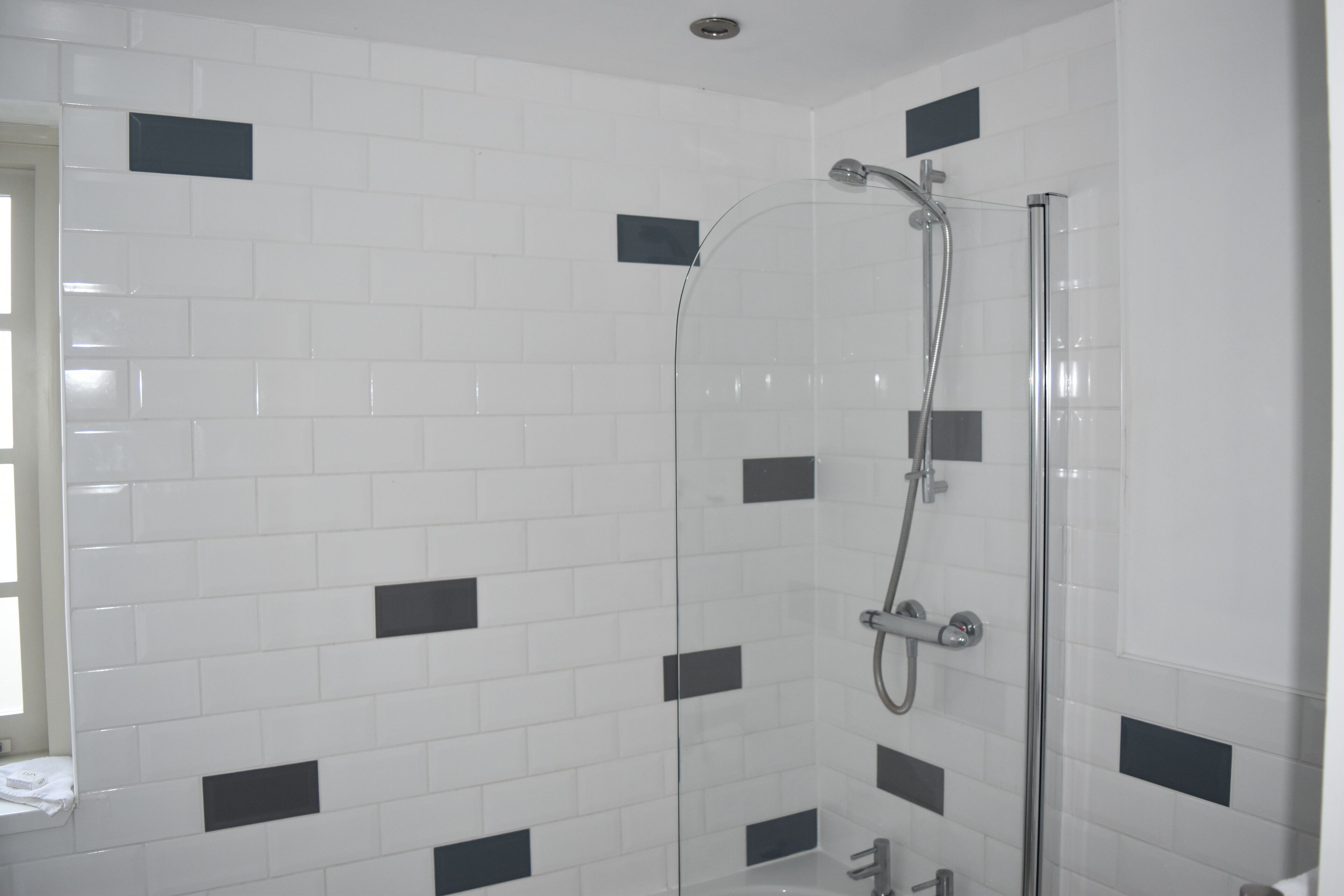 A shower with a glass door, white tiled walls with black accents, and a visible showerhead and faucet.