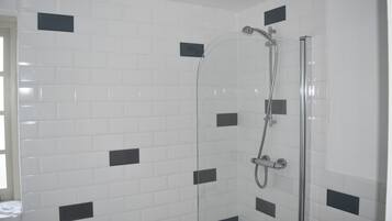 A shower with a glass door, white tiled walls with black accents, and a visible showerhead and faucet.