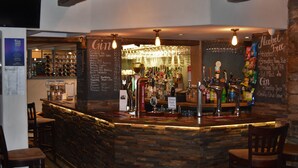 A bar area with a stone counter, multiple taps, and a variety of bottles and glasses. - Three Horseshoes (Barry)