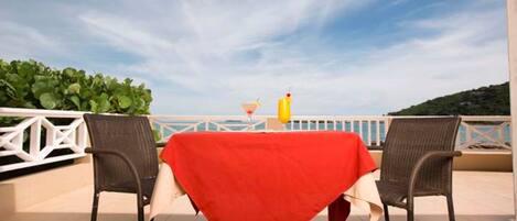 A terrace with a table covered in a red tablecloth, two wicker chairs, and a glass of orange juice.