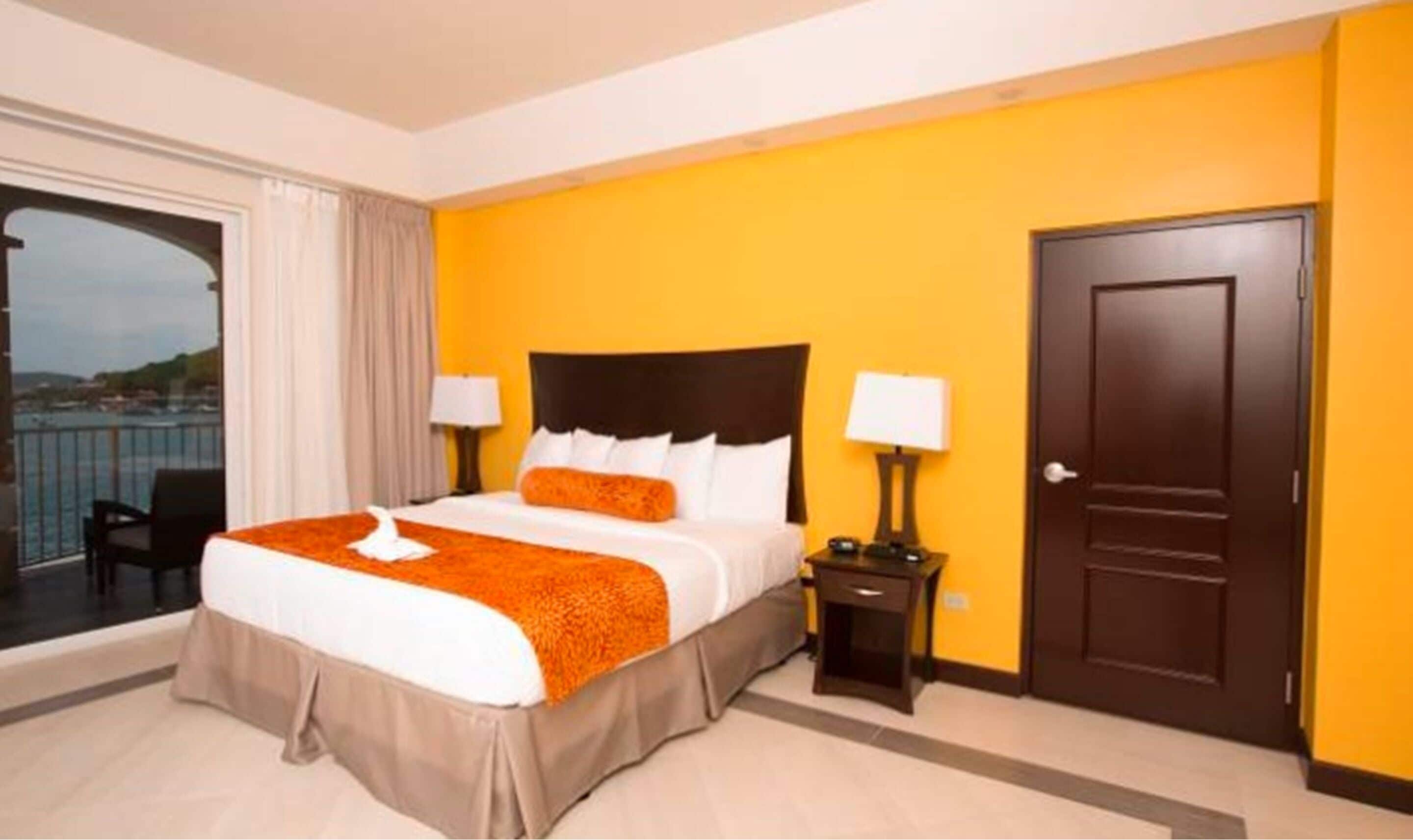 Quarto de hotel com uma cama, duas mesas de cabeceira, uma porta e vista para o mar.