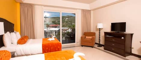 A hotel room with two beds, a TV, a chair, and a large window with a view of a town and hills.