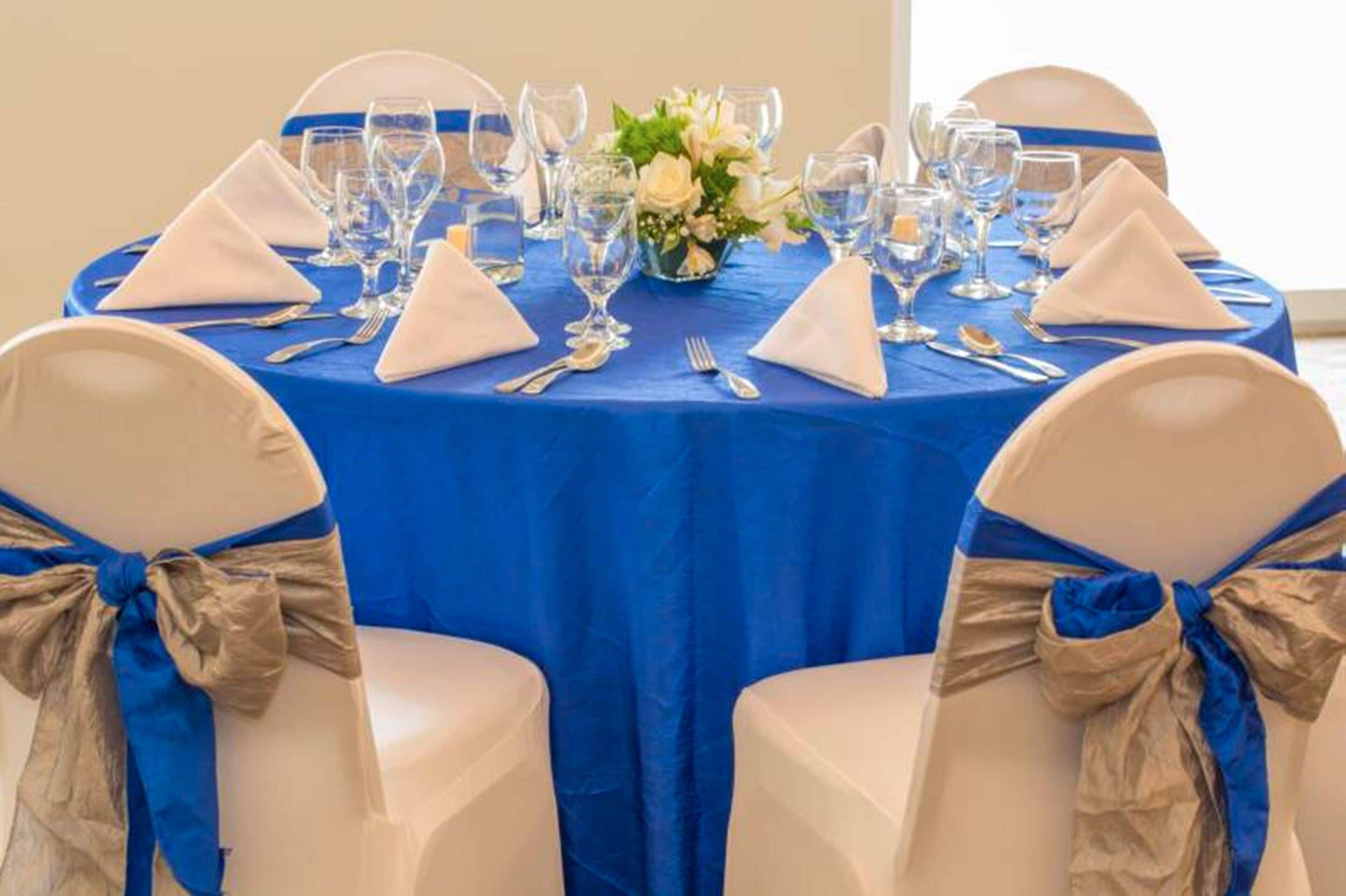 A round table with a blue tablecloth, white napkins, and a vase of flowers.