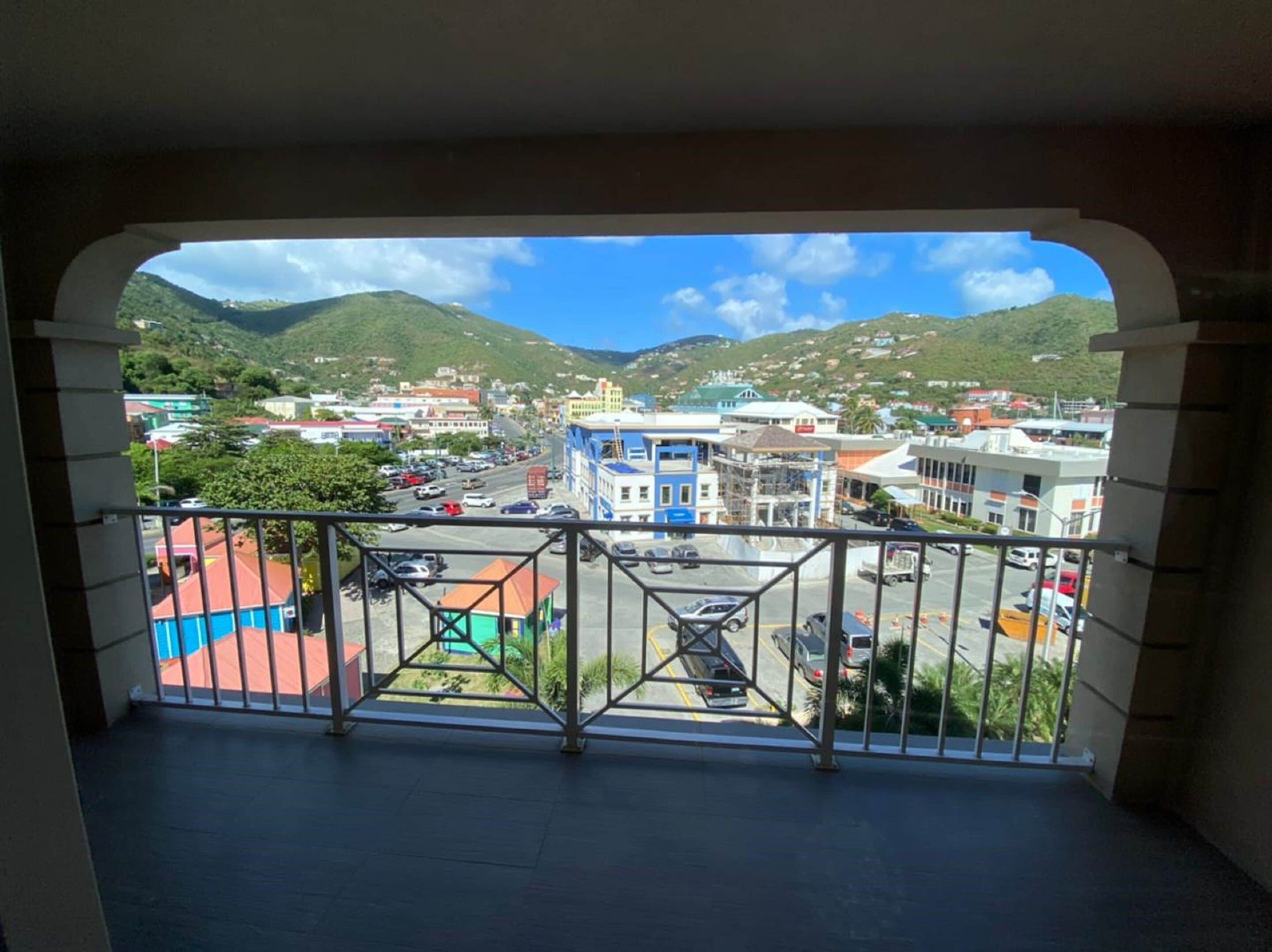 A balcony with a view of a town, buildings, and hills.