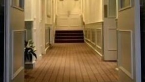 A hotel hallway with a wooden floor, a staircase, and a sign above the door.