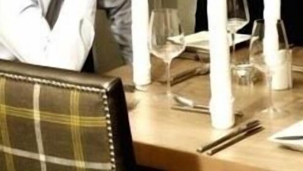 A dining table set with white napkins, wine glasses, and a bottle of wine.