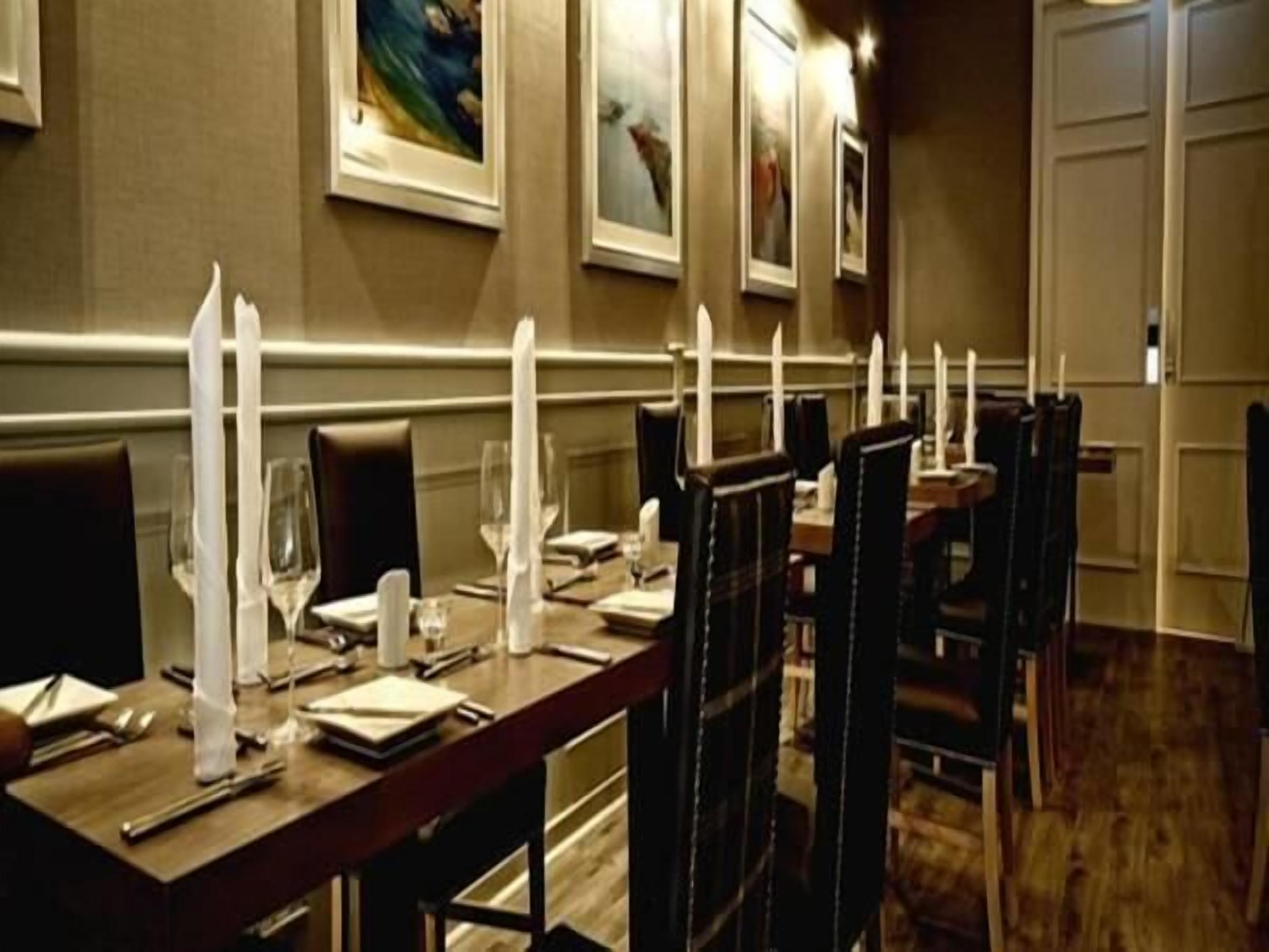 Un comedor con mesas dispuestas para el servicio, sillas y cuadros en las paredes.