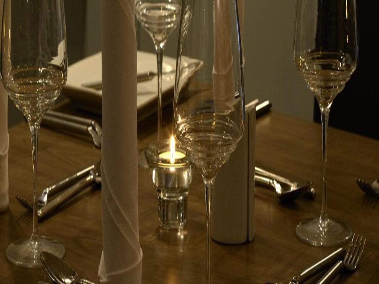 A table set for dining with wine glasses, cutlery, and a lit candle.
