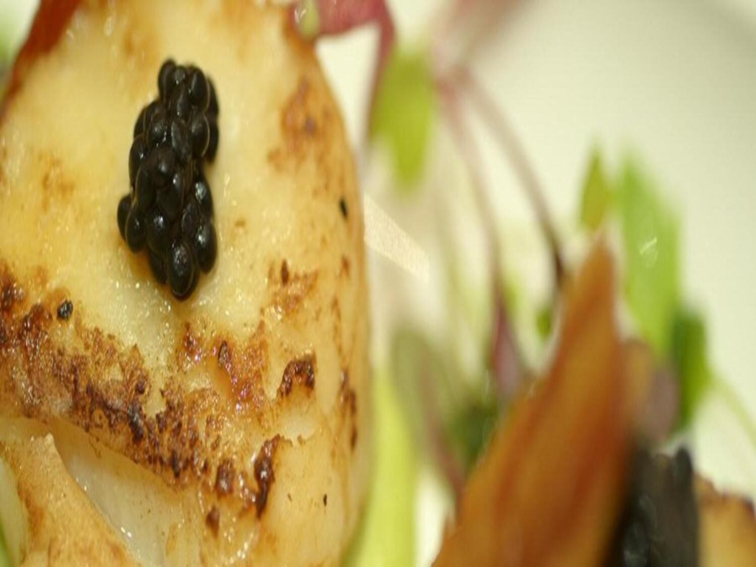 Primer plano de un vieiras sellada con un topping de caviar negro.
