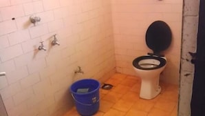 A small bathroom with a toilet, a blue bucket, and a wall-mounted faucet. - Vasco Residency (Marmagao)