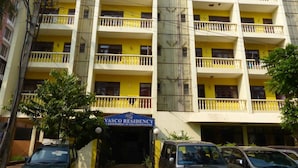 A multi-story residential building with balconies, a sign indicating it is a government undertaking, and several parked vehicles in front. - Vasco Residency (Marmagao)