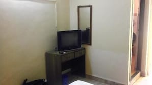 A small room with a television on a wooden stand, a mirror on the wall, and a door leading to another room. - Vasco Residency (Marmagao)