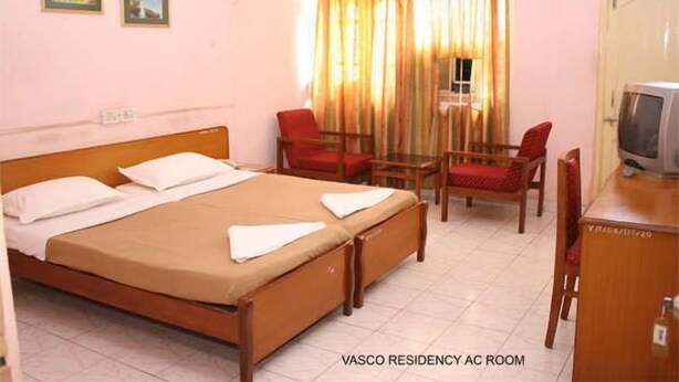 A room with a bed, two chairs, a desk, and a television. - Vasco Residency (Marmagao)