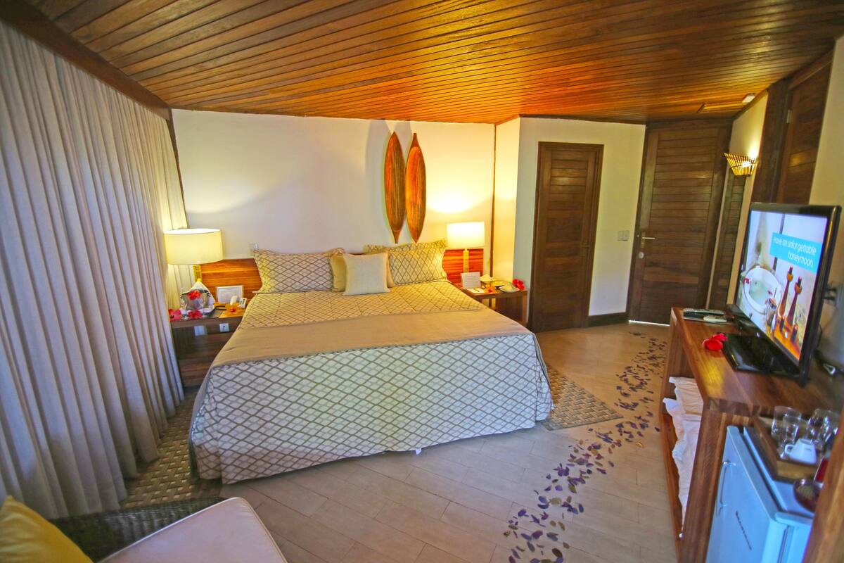 Une chambre d’hôtel avec un grand lit, une télévision, un bureau avec un ordinateur et un plafond en bois.