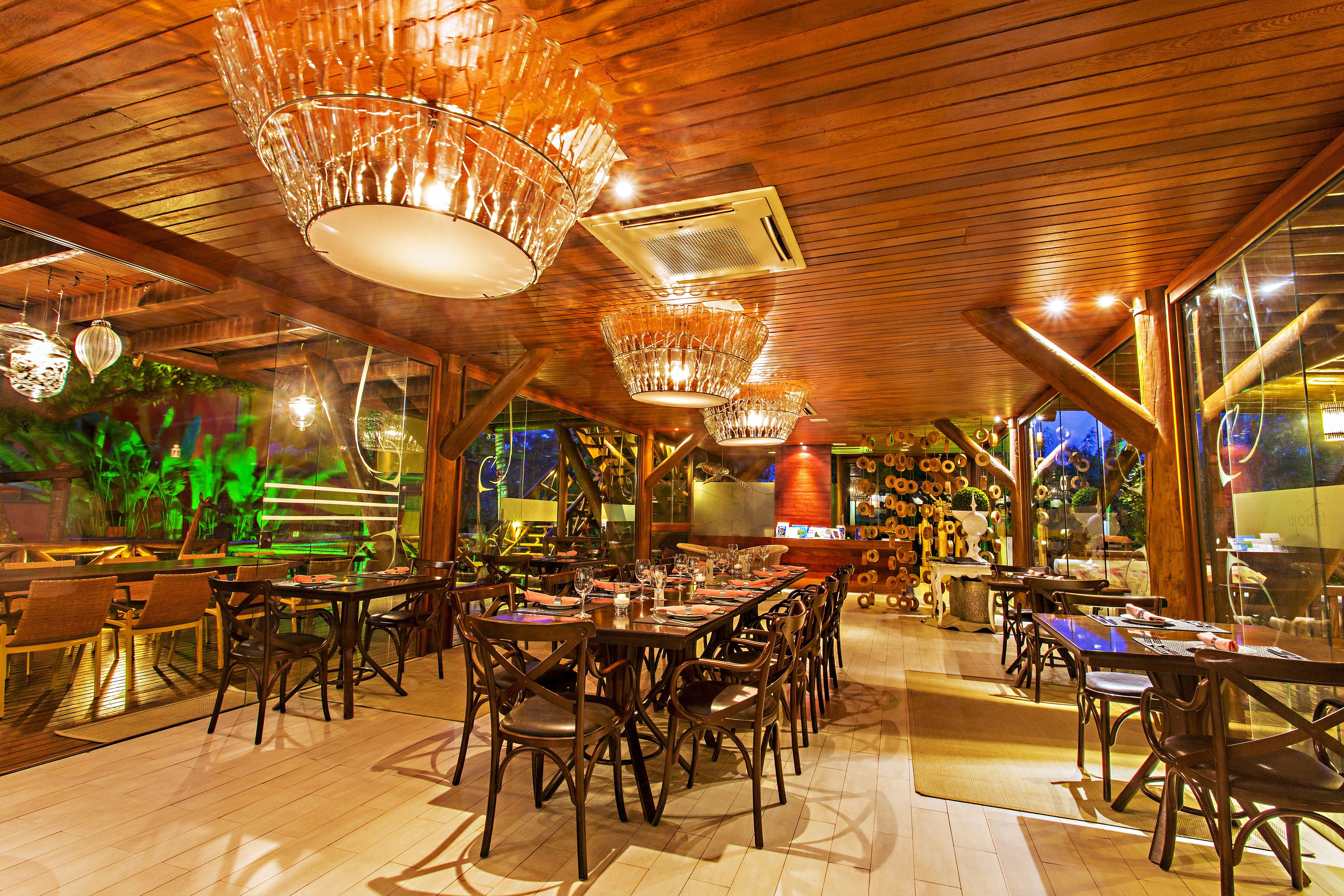 A restaurant with wooden ceiling and large windows, featuring multiple dining tables and chairs.