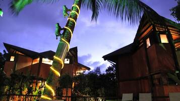 Experience the unique charm of our resort, where a spiral staircase wraps around a majestic palm tree, surrounded by modern buildings and an inviting outdoor seating area.