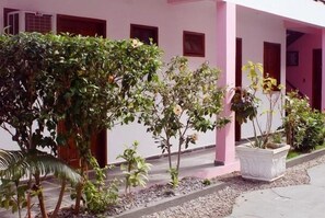 A building with pink walls and multiple windows. There are several potted plants and a palm tree in the foreground. - Bahiabacana Hotel (Porto Seguro)