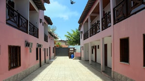 Une ruelle étroite bordée d’immeubles roses, avec un sol en pierre et une poubelle bleue.