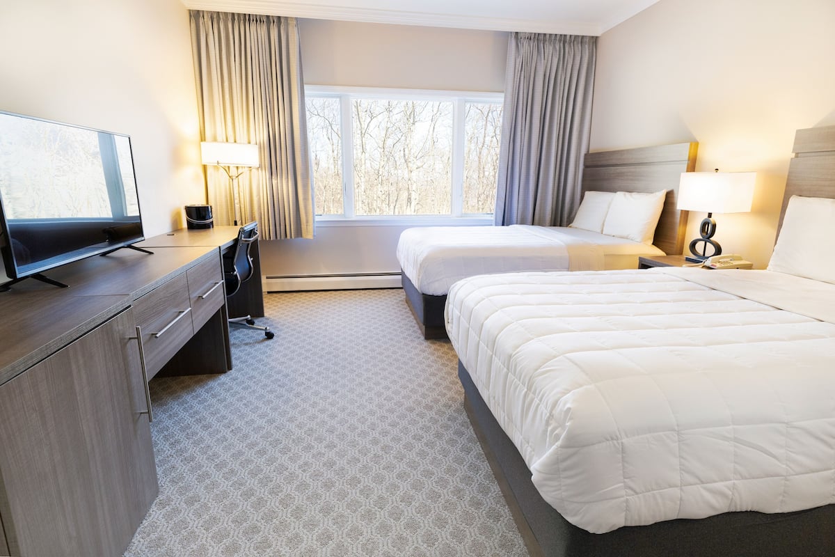 A hotel room with two beds, a desk with a TV, a lamp, and a window with curtains.