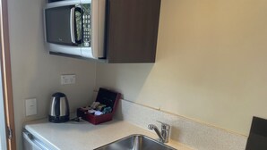 A compact kitchen with a stainless steel sink, a microwave, and a small red box with items. - Allan Court Motel (Dunedin)