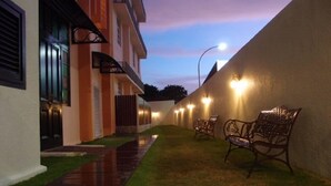A pathway leading to a building with a gated entrance, a small lawn area with benches, and a wall with lights. - G-Inn (George Town)