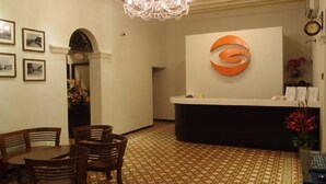 A reception area with a chandelier, a reception desk, framed pictures on the wall, and a patterned floor. - G-Inn (George Town)