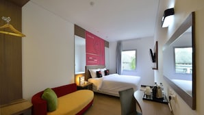 Een hotelkamer met een bed, een rood-geel sofa, een bureau met stoel, een televisie en een raam met uitzicht.