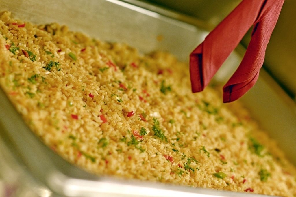 A tray of cooked rice with herbs and red peppers.