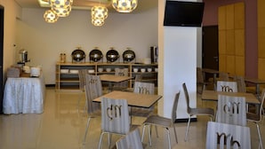 Een moderne eetruimte met ronde tafels en stoelen, decoratieve bolvormige lampen en een flatscreen televisie aan de muur.