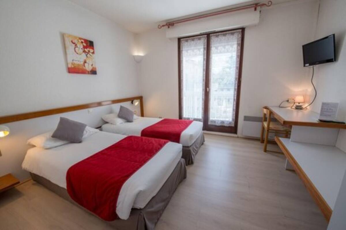 Une chambre d’hôtel avec deux lits, une télévision, un bureau et une fenêtre donnant sur un paysage agréable.