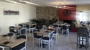 A restaurant with multiple tables and chairs, a stone wall, and a clock on the wall. - Hotel Les Cordeliers (Casteljaloux)