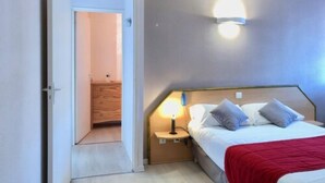 A bedroom with a bed, bedside table, lamp, and a red throw blanket. - Hotel Les Cordeliers (Casteljaloux)