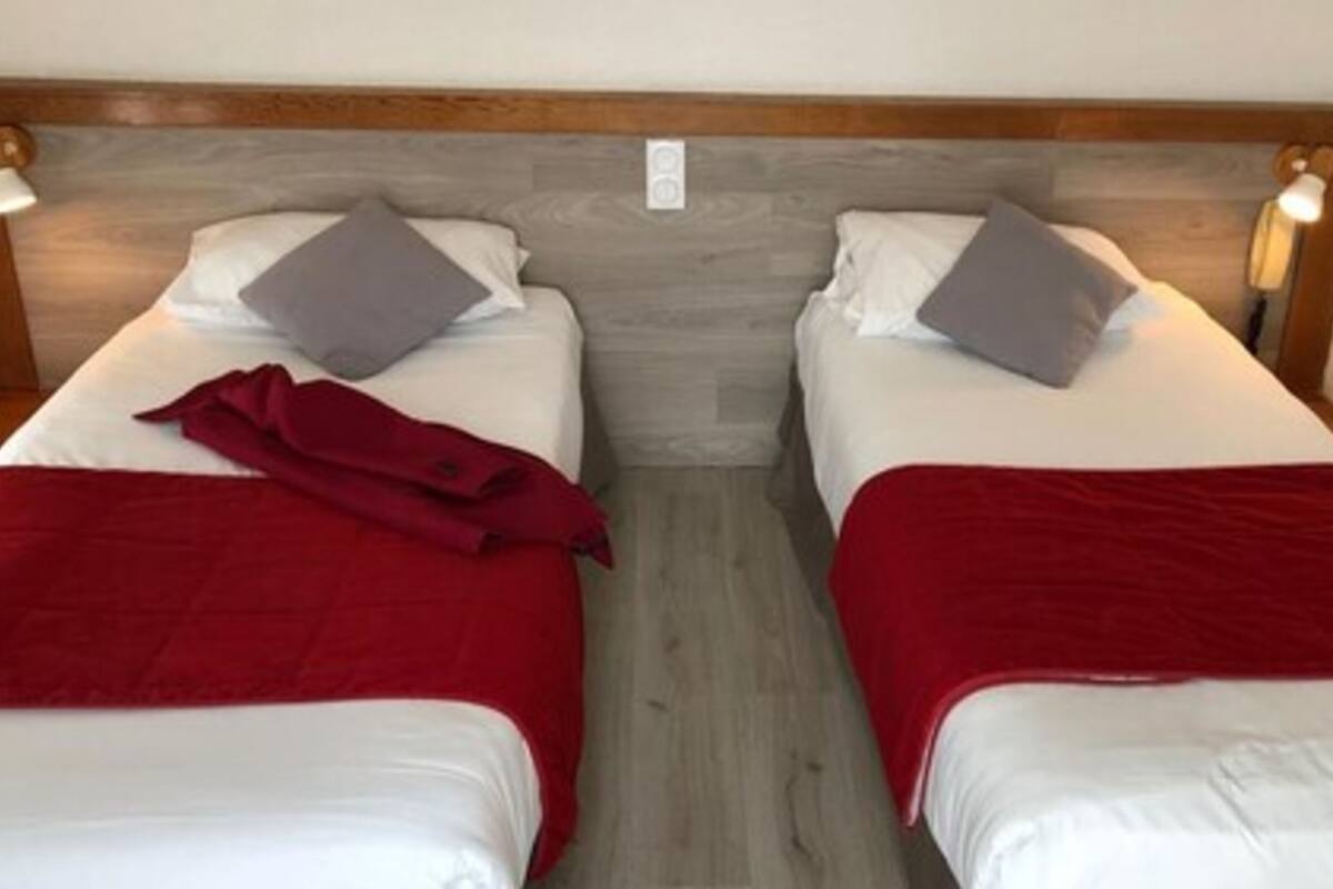 Deux lits simples avec des têtes de lit en bois, du linge de lit blanc et des couvertures rouges.